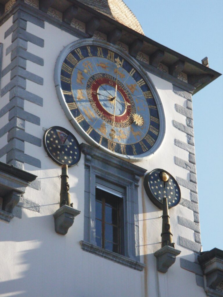 Astronomische Uhr am Rathaus Sitten / Sion - Foto: Lysippos, https://commons.wikimedia.org/wiki/User:Lysippos - Lizenz: https://creativecommons.org/licenses/by-sa/3.0/deed.en - Datei: https://de.wikipedia.org/wiki/Sitten#/media/Datei:Sion,_h%C3%B4tel_de_ville,_horologe_astronomique_-_ch.jpg