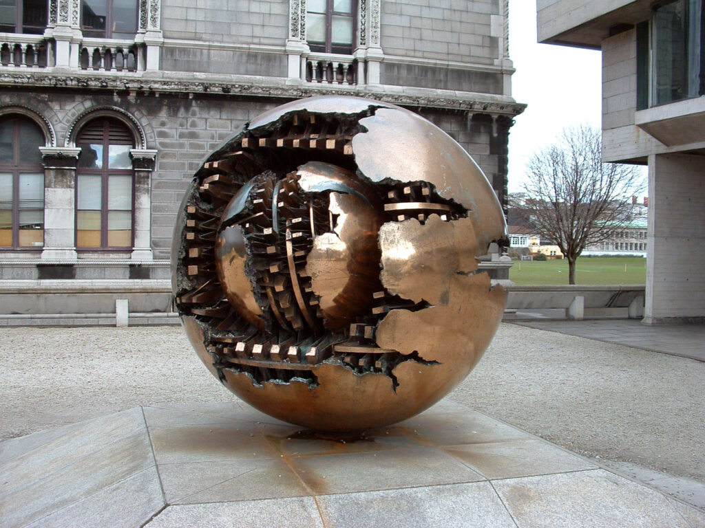 Arnaldo Pomodoro's Sphere Within Sphere sculpture stands outside the Berkeley Library, Trinity University, Dublin, Ireland, 2006 - Foto: https://en.wikipedia.org/wiki/User:Jasonm - Lizenz: https://creativecommons.org/licenses/by-sa/2.5/deed.en - Datei: https://commons.wikimedia.org/wiki/File:Trinity_Pomodoro.jpg