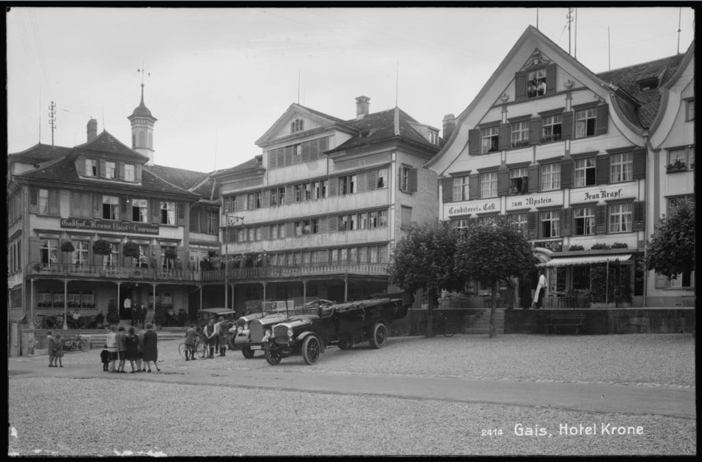 Dorfplatz Gais, Hotel Krone mit singendem Chor auf Balkon, Café Conditorei zum Alpstein und Automobilen im Jahr 1927 (Staatsarchiv Appenzell Ausserrhoden, Ja.011-01-03-010-019)