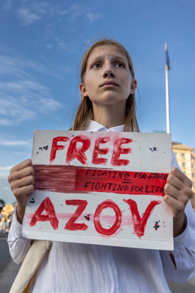 Kiew – 28.07.2024: Eine junge Teilnehmerin hält während einer Solidaritätsaktion ein handgemaltes Plakat mit der Aufschrift „Free Azov“. Die Demonstration steht im Zeichen der Forderung nach der Freilassung ukrainischer Soldaten, die von Russland gefangen gehalten werden © Patrick Lüthy / ukrainianphotodiary.org