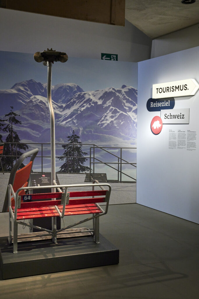 Der Eingangsbereich der Ausstellung empfängt die Besucherinnen und Besucher mit einem Zweiersessellift vom Sattel-Hochstuckli und einer Audiostation, die sie gleich in die Rolle von Touristinnen und Touristen versetzt. Der Lift war von 1950 bis 2005 in Betrieb. © Schweizerisches Nationalmuseum ǀ Foto: Mara Truog