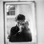 Die Kunstkritikerin Maria Netter mit Kamera im Spiegel - Foto: © Maria Netter, SIK-ISEA, Courtesy Fotostiftung Schweiz - https://recherche.sik-isea.ch/de/sik:document-14064678/in/sikisea/document/tiles?0.0.type=document&0.0.q=maria%20netter&0.type=document