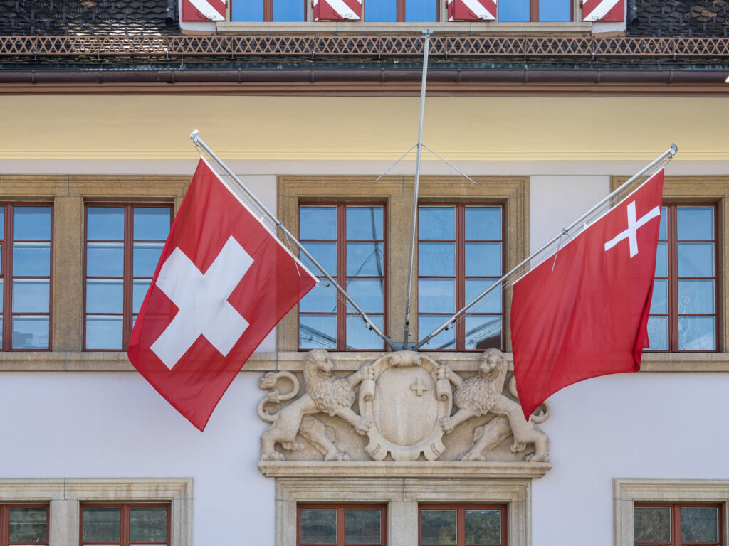 Schweizerfahne und Schwyzerfahne am Regierungsgebäude in Schwyz - Foto: JoachimKohler-HB, https://commons.wikimedia.org/wiki/User:JoachimKohler-HB - Lizenz: https://creativecommons.org/licenses/by-sa/4.0/deed.en - Datei: https://commons.wikimedia.org/wiki/File:Schweizer_und_Schwyzer_Fahnen_(Schwyz,_2022).jpg