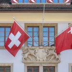 Schweizerfahne und Schwyzerfahne am Regierungsgebäude in Schwyz - Foto: JoachimKohler-HB, https://commons.wikimedia.org/wiki/User:JoachimKohler-HB - Lizenz: https://creativecommons.org/licenses/by-sa/4.0/deed.en - Datei: https://commons.wikimedia.org/wiki/File:Schweizer_und_Schwyzer_Fahnen_(Schwyz,_2022).jpg